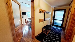 Un pasillo con suelo de madera, una zona con baldosas blanco y negro, un banco y un perchero con ganchos.