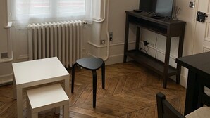 Ein Zimmer mit einer weißen Heizung, einem Fernseher auf einem Holzboden, einem kleinen weißen Tisch und einem Stuhl.