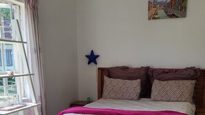 A bedroom with a bed, a window, a star decoration, and a painting on the wall. - African Violet (Mbabane)