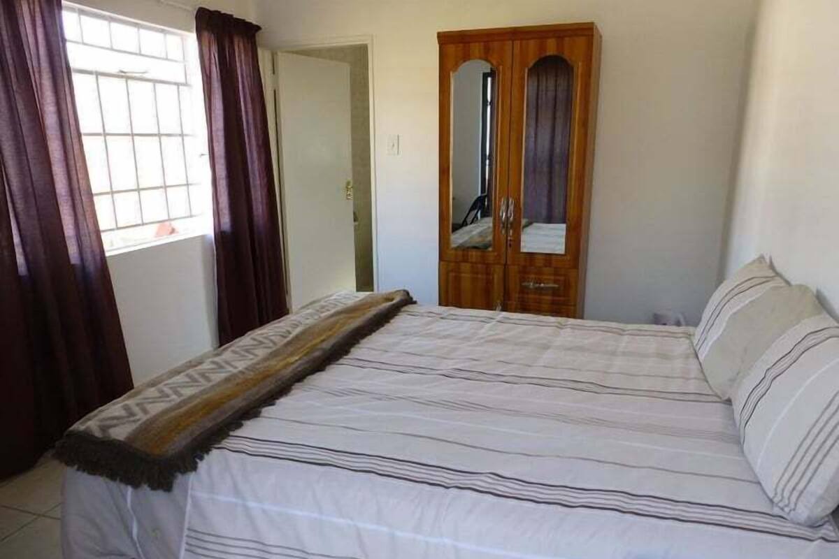 Quarto com cama, guarda-roupa de madeira, espelho e janela com cortinas.