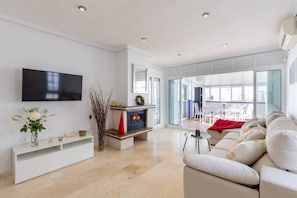 A modern living room with a flat-screen TV, a fireplace, a sofa, and a dining area with a view. - Infinity Haven by Fidalsa (Villamartín)