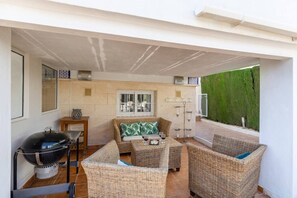 A covered outdoor seating area with wicker furniture, a grill, and a view of a green hedge. - Infinity Haven by Fidalsa (Villamartín)