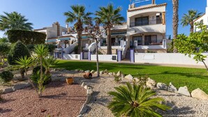 A multi-story residential building with a well-maintained garden, palm trees, and a clear blue sky. - Infinity Haven by Fidalsa (Villamartín)