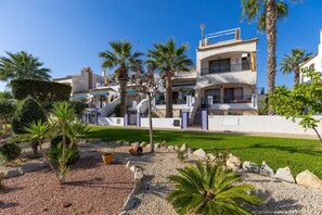 A multi-story residential building with a well-maintained garden, palm trees, and a clear blue sky. - Infinity Haven by Fidalsa (Villamartín)