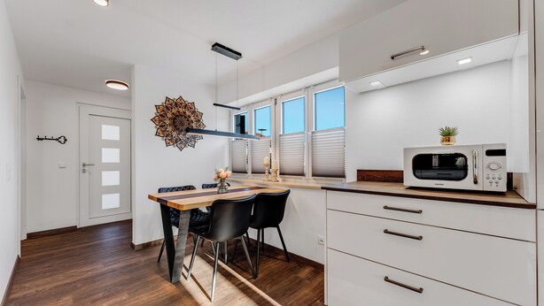Una cocina moderna con armarios blancos, un microondas y un comedor con mesa de madera y sillas negras.