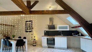 A modern kitchen with white cabinetry, a built-in oven, and a microwave. There is a dining area with a white table and black chairs. The room has exposed wooden beams and a skylight. - Superb furnished and equipped T3 decorated for the festive season (Montluçon)