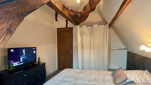 A bedroom with a sloped ceiling, a bed with a patterned blanket, a dresser, a television, and a door with curtains. - Superb furnished and equipped T3 decorated for the festive season (Montluçon)