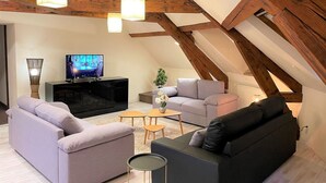 An attic living room with exposed wooden beams, a black entertainment unit, and two sofas. - Superb furnished and equipped T3 decorated for the festive season (Montluçon)
