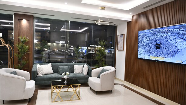 A modern living room with a large TV, a sofa, two armchairs, and a coffee table. - Pestana Apartment 4 (Riyadh)