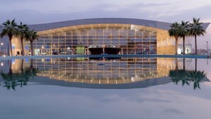 A modern building with a glass facade, palm trees, and a reflective pool in front. - Pestana Apartment 4 (Riyadh)