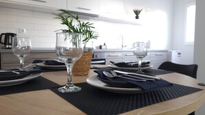 A dining table set with plates, cutlery, and wine glasses, with a potted plant and a woven basket in the background. - Elite Apartment Larisa (Larissa)