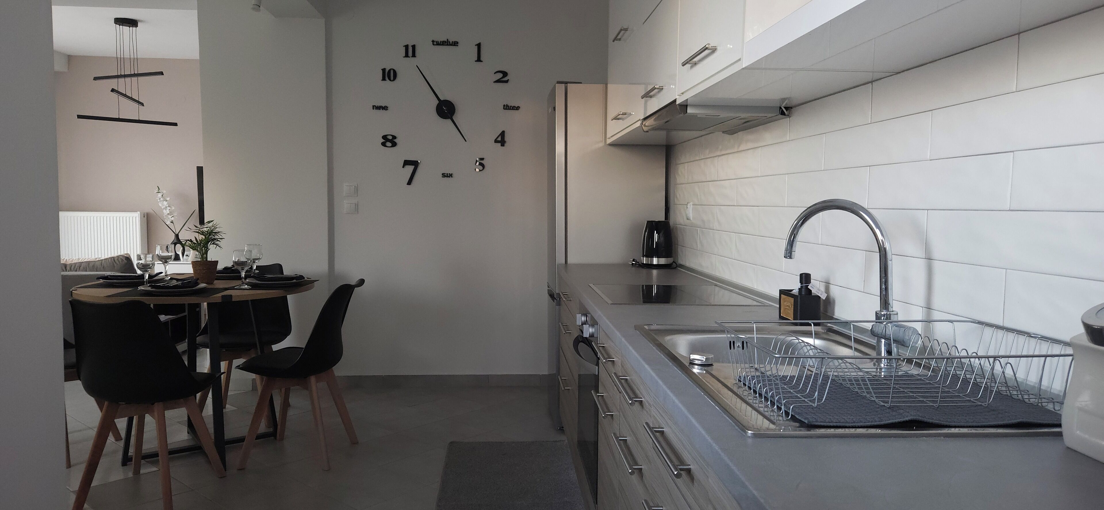 A modern kitchen with a built-in clock, stainless steel appliances, and a dining area with a table and chairs.