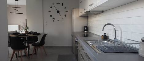 A modern kitchen with a built-in clock, stainless steel appliances, and a dining area with a table and chairs.