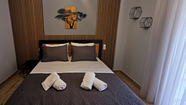 A neatly made bed with a dark patterned bedspread, two pillows, and two rolled towels on the bed. - Elite Apartment Larisa (Larissa)