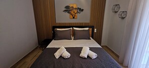A neatly made bed with a dark patterned bedspread, two pillows, and two rolled towels on the bed. - Elite Apartment Larisa (Larissa)