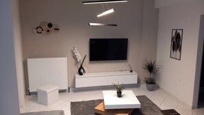 A modern living room with a white sofa, a coffee table, a TV, and a radiator. - Elite Apartment Larisa (Larissa)