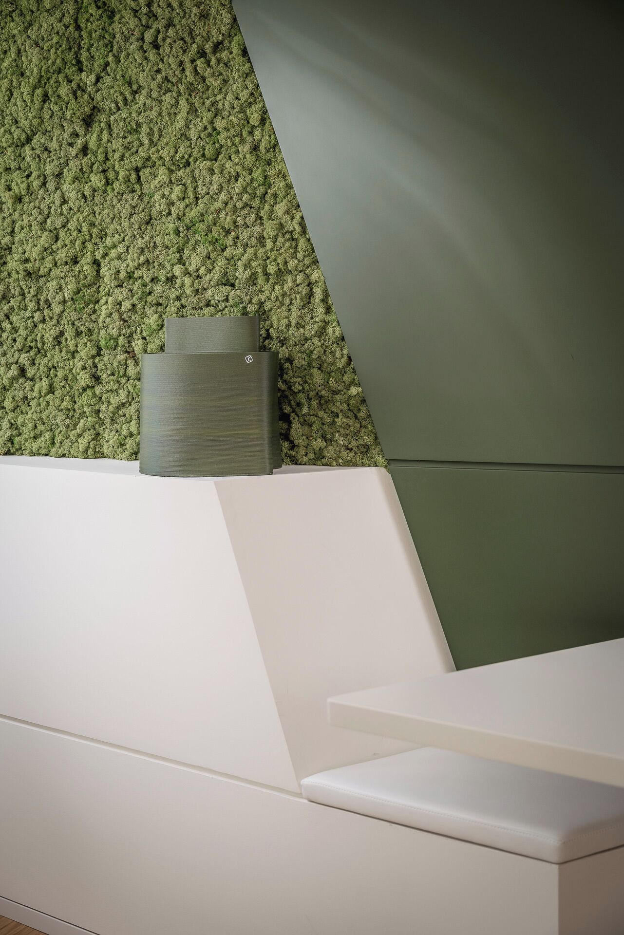 A modern reception desk with a green textured wall and a white counter.