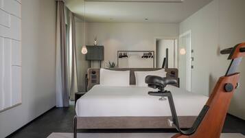 A modern bedroom with a large bed, a desk with a chair, a treadmill, and a mirror.