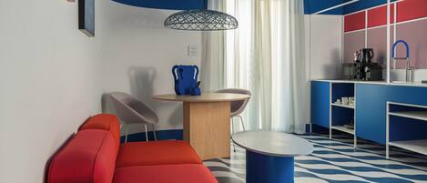 Una habitación moderna con un sofá rojo, una mesa redonda y una zona de cocina con cafetera.