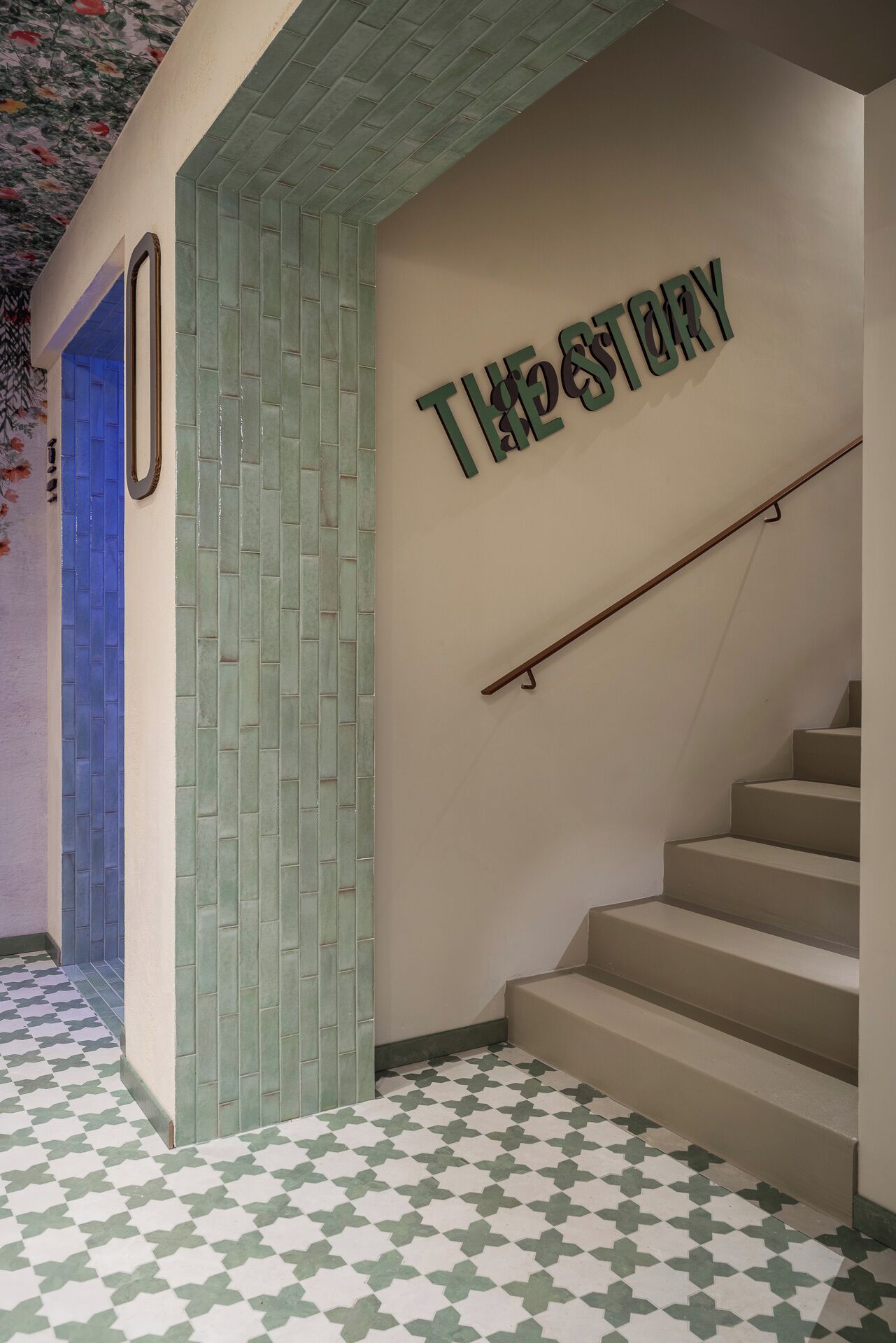 Eine Treppe mit Handlauf, eine Wand mit dem Schriftzug „THE STORY“ und eine Tür mit blauem Rahmen.