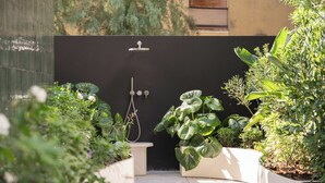A modern outdoor shower area with a black wall, surrounded by lush greenery and potted plants. - Mode Eco Mood Hotel (Rimini)