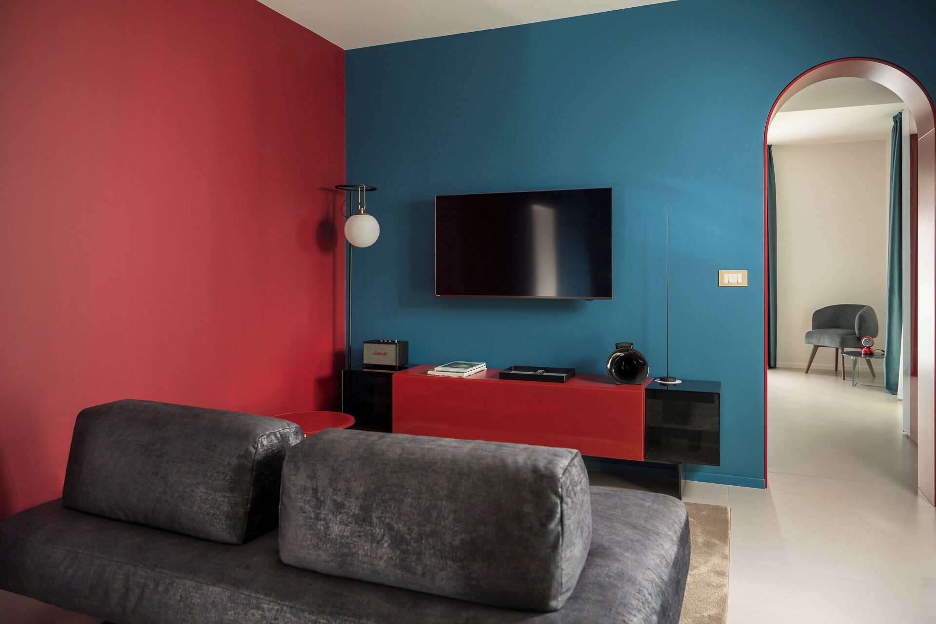 En moderne stue med røde og blå farver, et fladskærms-tv, en sofa, et sofabord og et konsolbord med lampe og radio.