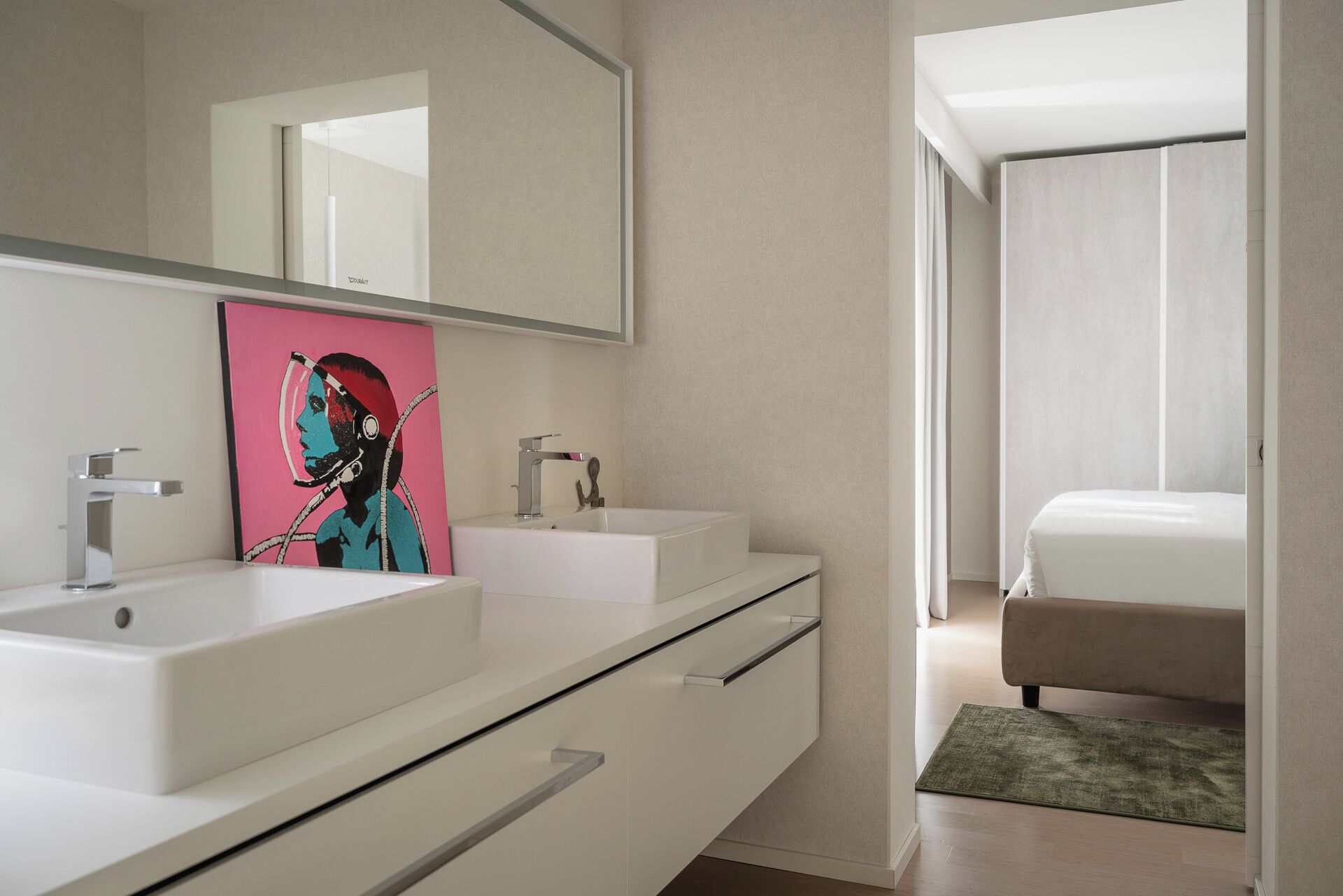 A modern bathroom with two sinks, a large mirror, and a painting of a woman with headphones.