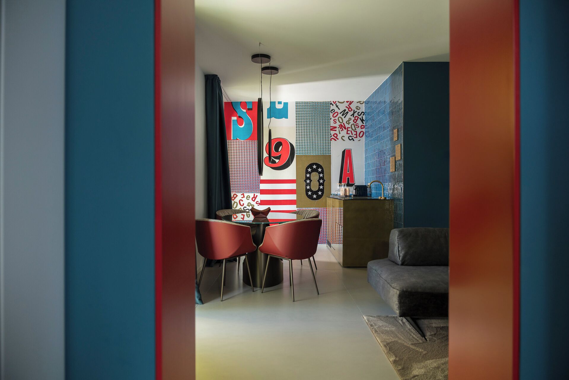 A modern living room with a sofa and a dining area with two red chairs.