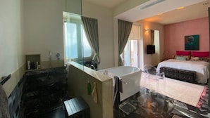 A modern hotel room with a large bathtub, a separate shower area, a bed with a pink headboard, and a large mirror. - Exclusive Duplex Penthouse with Jacuzzi and Panoramic Views in Valletta  (Sliema)