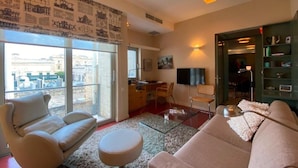 A spacious living room with a large window, a sofa, a coffee table, and a television. - Exclusive Duplex Penthouse with Jacuzzi and Panoramic Views in Valletta  (Sliema)