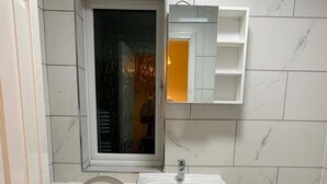 Un baño con lavamanos blanco, espejo y puerta de ducha.
