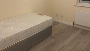 Un dormitorio con una cama individual, suelo de madera clara, un radiador y una ventana.