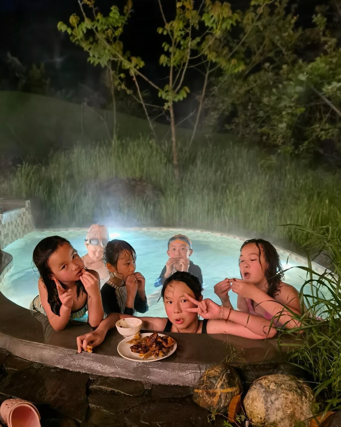 A group of people in a hot tub surrounded by greenery at night.