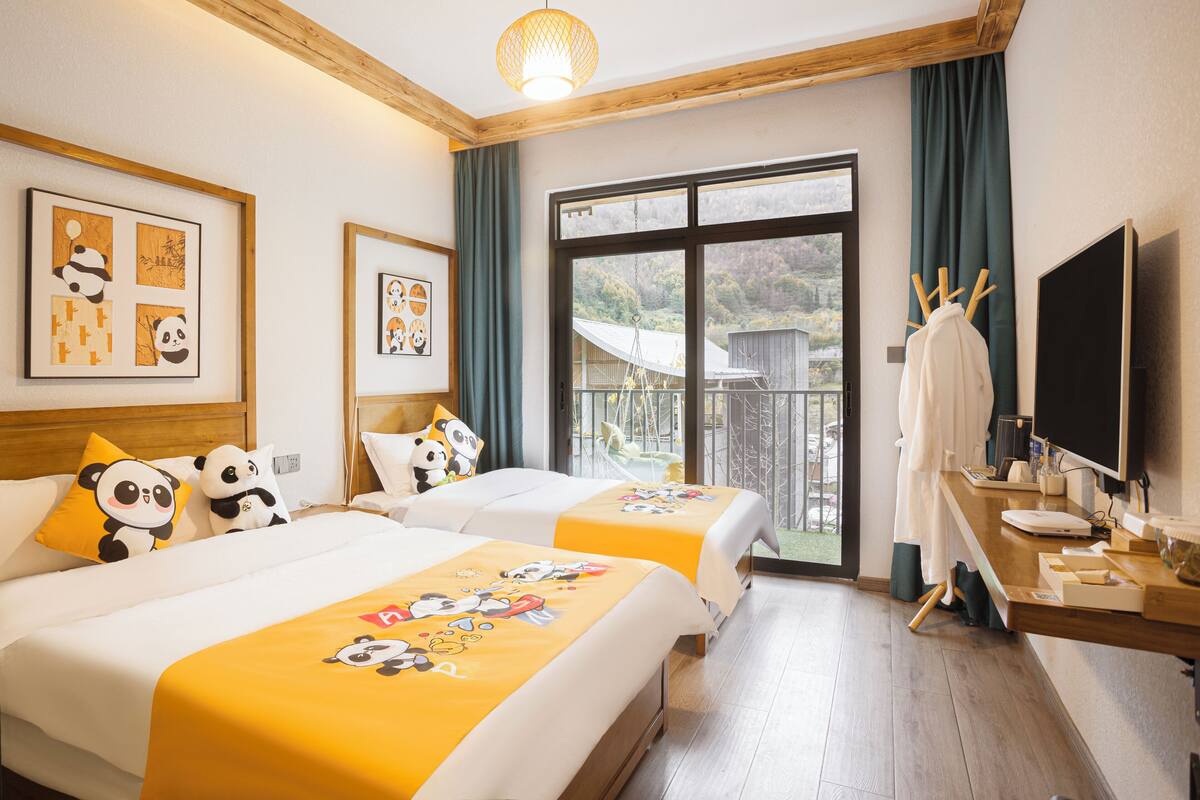 Habitación de hotel con dos camas, decoración temática de panda, un balcón con vistas y un televisor en la cómoda.