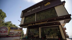 Een modern hotel en restaurant genaamd 'The Origin', met een opvallend bord en grote ramen.