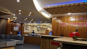 Een hotel receptie met een houten balie, een bank en een muur met de tekst 'THE ORIGIN'.