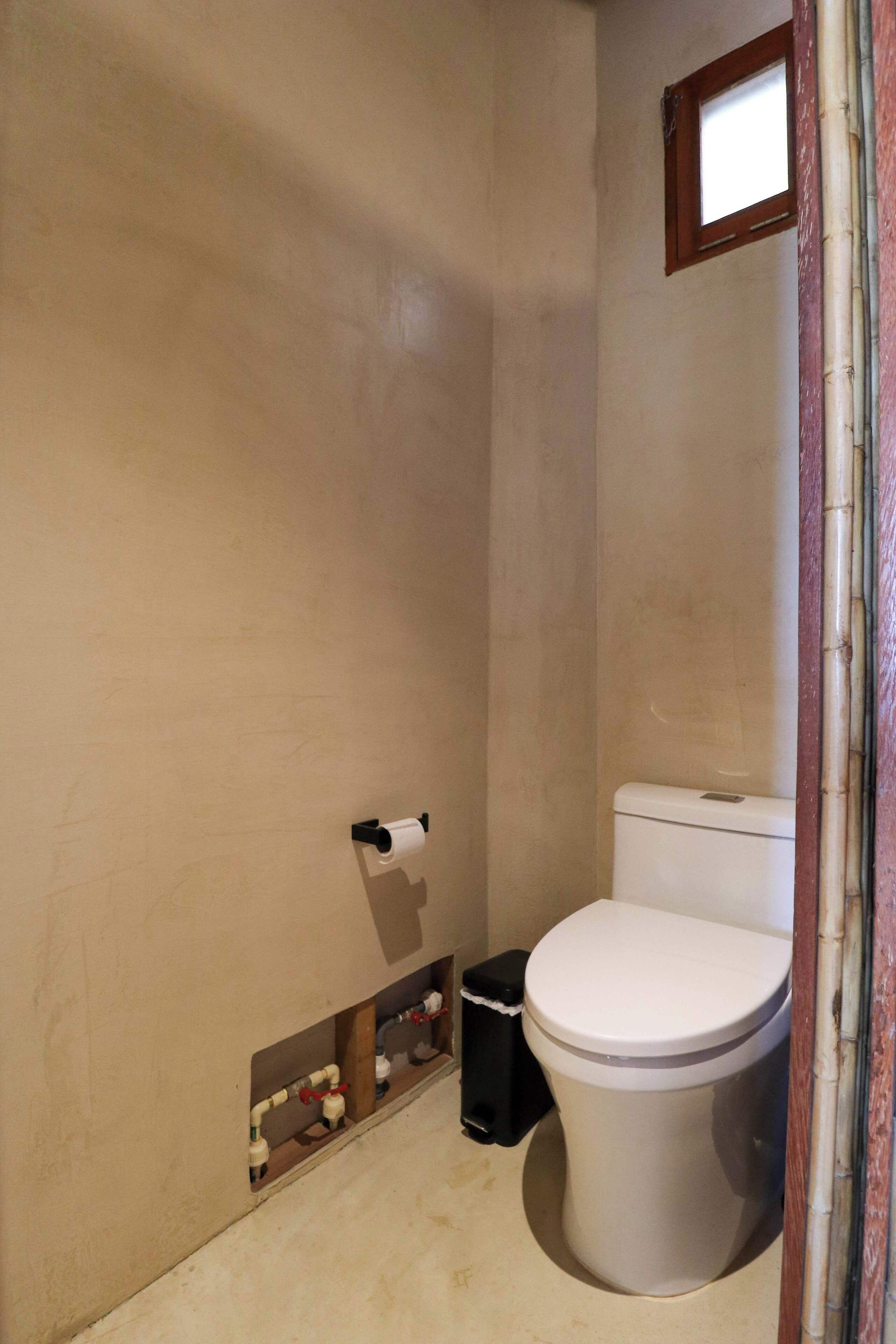Een badkamer met een toilet, een klein raam en een prullenbak.