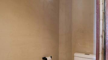 Een badkamer met een toilet, een klein raam en een prullenbak.