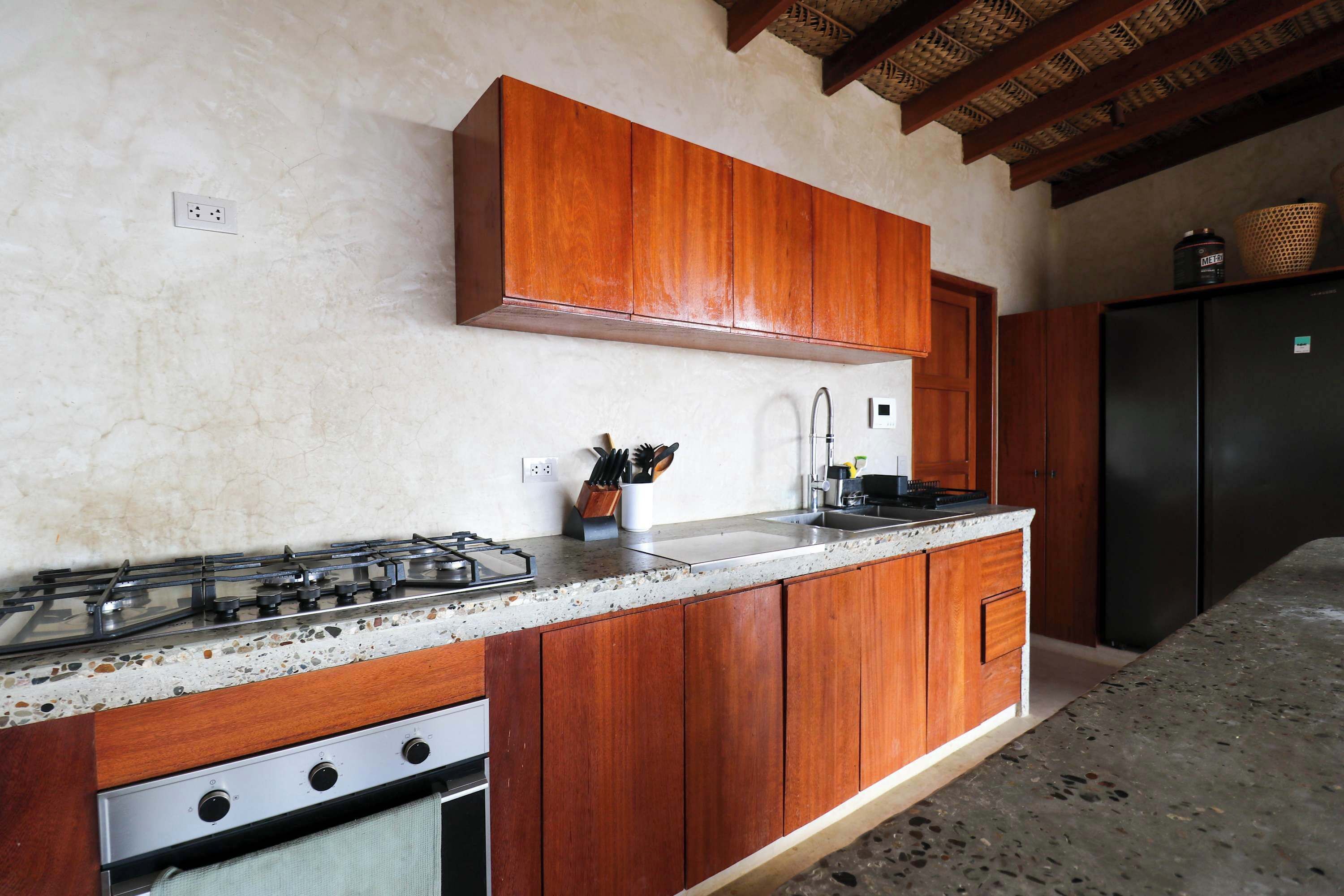 Une cuisine avec des meubles de rangement en bois, une cuisinière à gaz, un évier et un réfrigérateur noir.