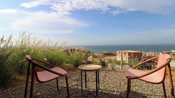 Two chairs and a small table on a gravel patio with a view of the sea and buildings in the background.