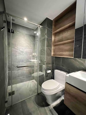 A modern bathroom with a glass-enclosed shower, a toilet, and wooden cabinetry. - Saigon Royal View Residence & River (Ho Chi Minh City)