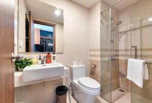 A modern bathroom with a glass-enclosed shower, a white sink with toiletries, and a toilet. - Saigon Royal View Residence & River (Ho Chi Minh City)