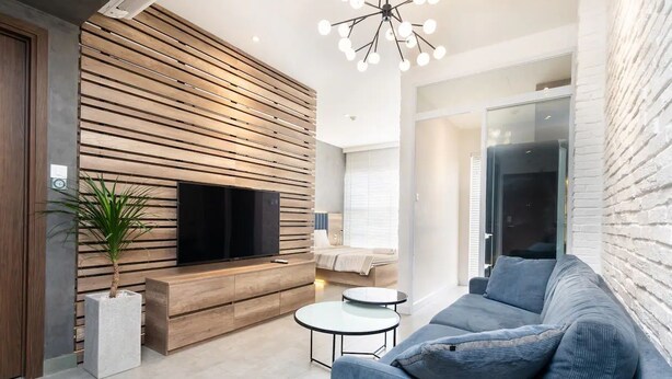A modern living room with a flat-screen TV, wooden slat wall, and a blue sofa. - Saigon Royal View Residence & River (Ho Chi Minh City)