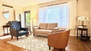 Ein Wohnzimmer mit einem beigen Sofa, einem dunklen Sessel und einem gemusterten Teppich.
