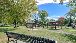 Ein Park mit einer Holzbank, Picknicktischen und überdachten Bereichen.