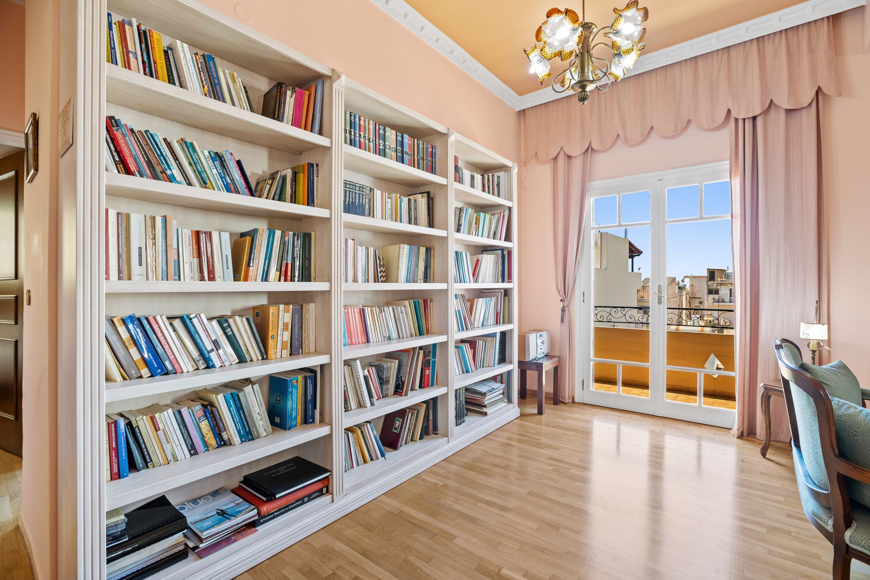 A spacious room with a large bookshelf filled with books, a wooden floor, and a view through a glass door to an outdoor area.