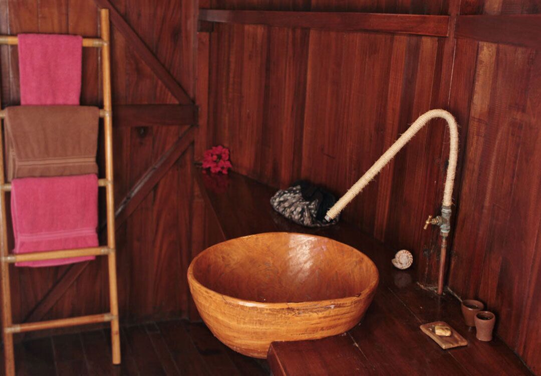 Una bañera de madera con un lavamanos de madera, una escalera de madera con toallas, y un taburete pequeño de madera.