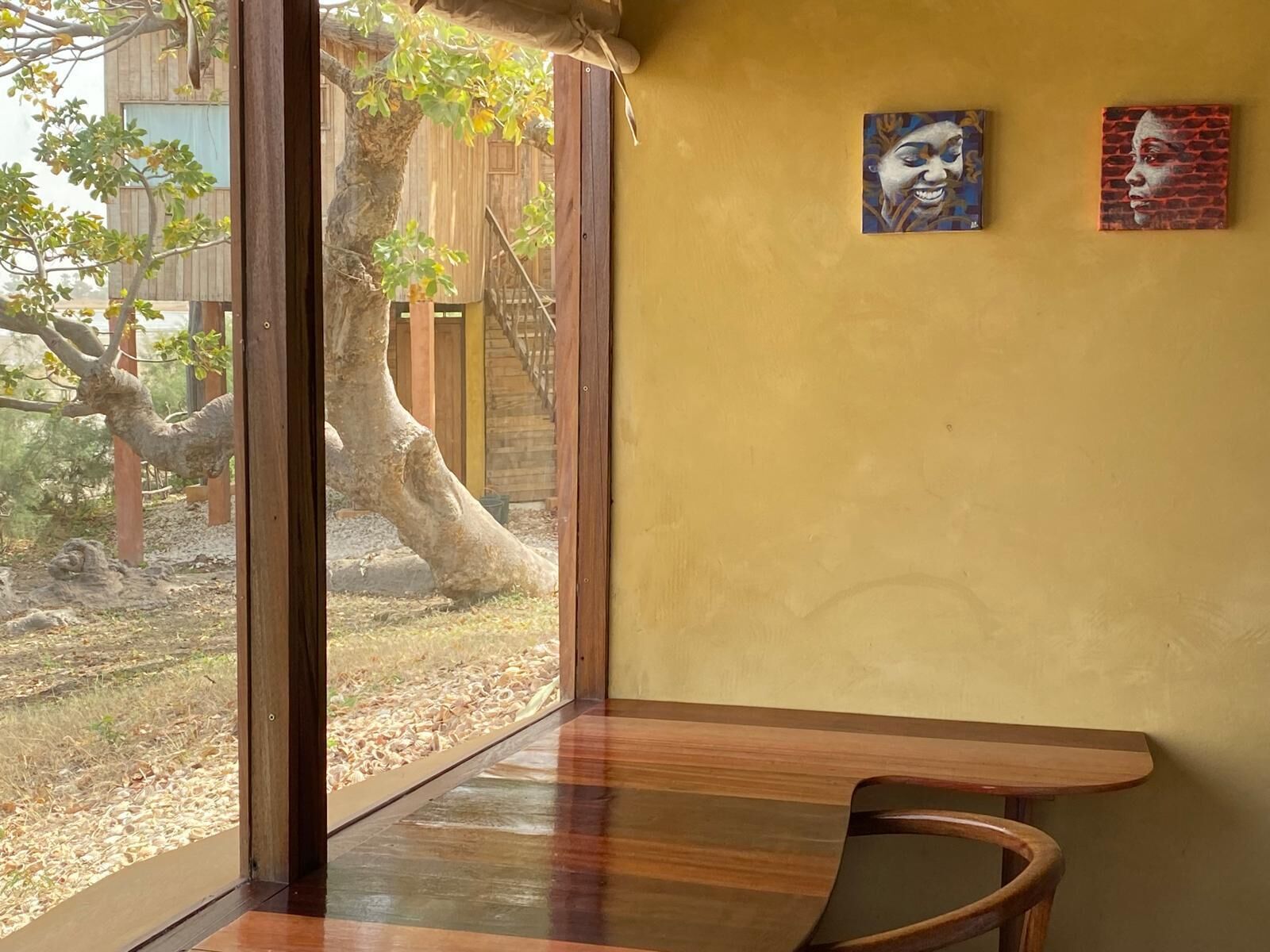 Una habitación con un ventanal grande, un banco de madera y dos cuadros en la pared.