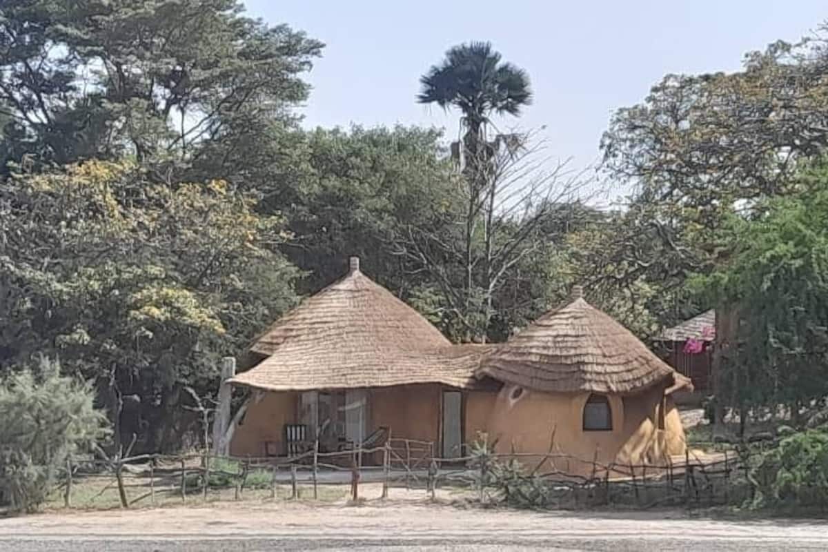 Eine traditionelle Hütte mit einem Reetdach und einem eingezäunten Bereich, umgeben von dichtem Grün und Bäumen.