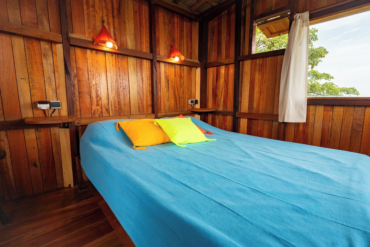Ein Zimmer mit Holzboden, einem Bett, zwei Wandlampen und einem Fenster mit Vorhang.